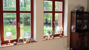 A room with two large windows, a wooden cabinet, and a small table with a lamp and a clock.