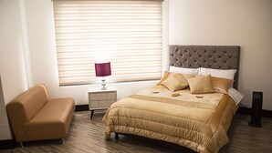 Une chambre à coucher avec un lit, une table de chevet, une lampe, une chaise et une fenêtre avec des stores.