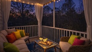 A covered outdoor seating area with a ceiling fan, string lights, and a view of trees.