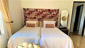 A double bed with a floral headboard, a bedside table with a mirror, and a tufted ottoman. - Cosy studio with kitchenette in Norton - 2120 (Norton)