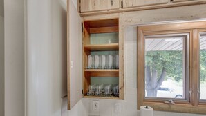 A kitchen with wooden cabinets, a window with a view of trees, and a countertop with a paper towel holder. - Cozy Westminster Retreat ~ Hot Tub ~ Near Denver ~ Spacious Yard (Westminster)
