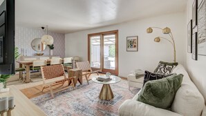 A modern living room with a dining area, a sofa, a coffee table, and a TV. - Cozy Westminster Retreat ~ Hot Tub ~ Near Denver ~ Spacious Yard (Westminster)