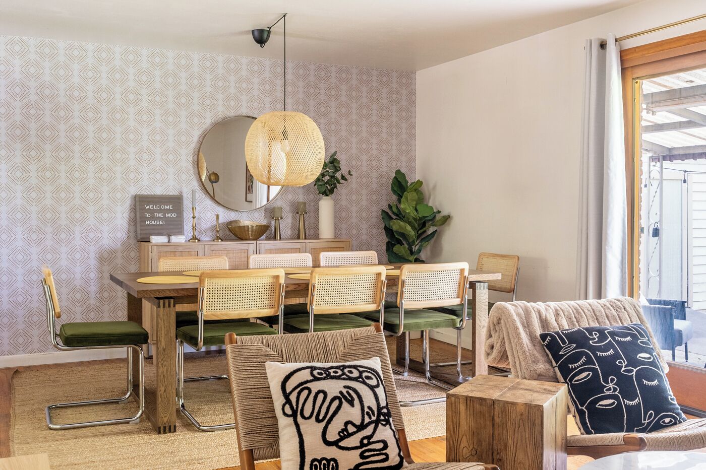 Uma área de refeições com uma mesa redonda, várias cadeiras, um lustre e uma placa de boas-vindas.