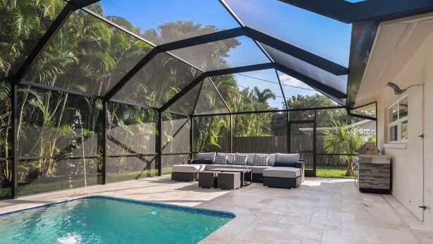 A covered outdoor pool area with a built-in seating area and a view of the surrounding greenery. - Naples Dream Escape 4BR Home, heated pool, 10min from Beach (Naples)