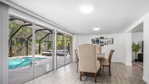 A spacious room with a large sliding glass door leading to a pool area, a dining table with chairs, and a ceiling light. - Naples Dream Escape 4BR Home, heated pool, 10min from Beach (Naples)