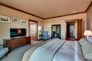 Un dormitorio con una cama grande, un televisor sobre un mueble de madera, una silla y cuadros enmarcados en la pared.