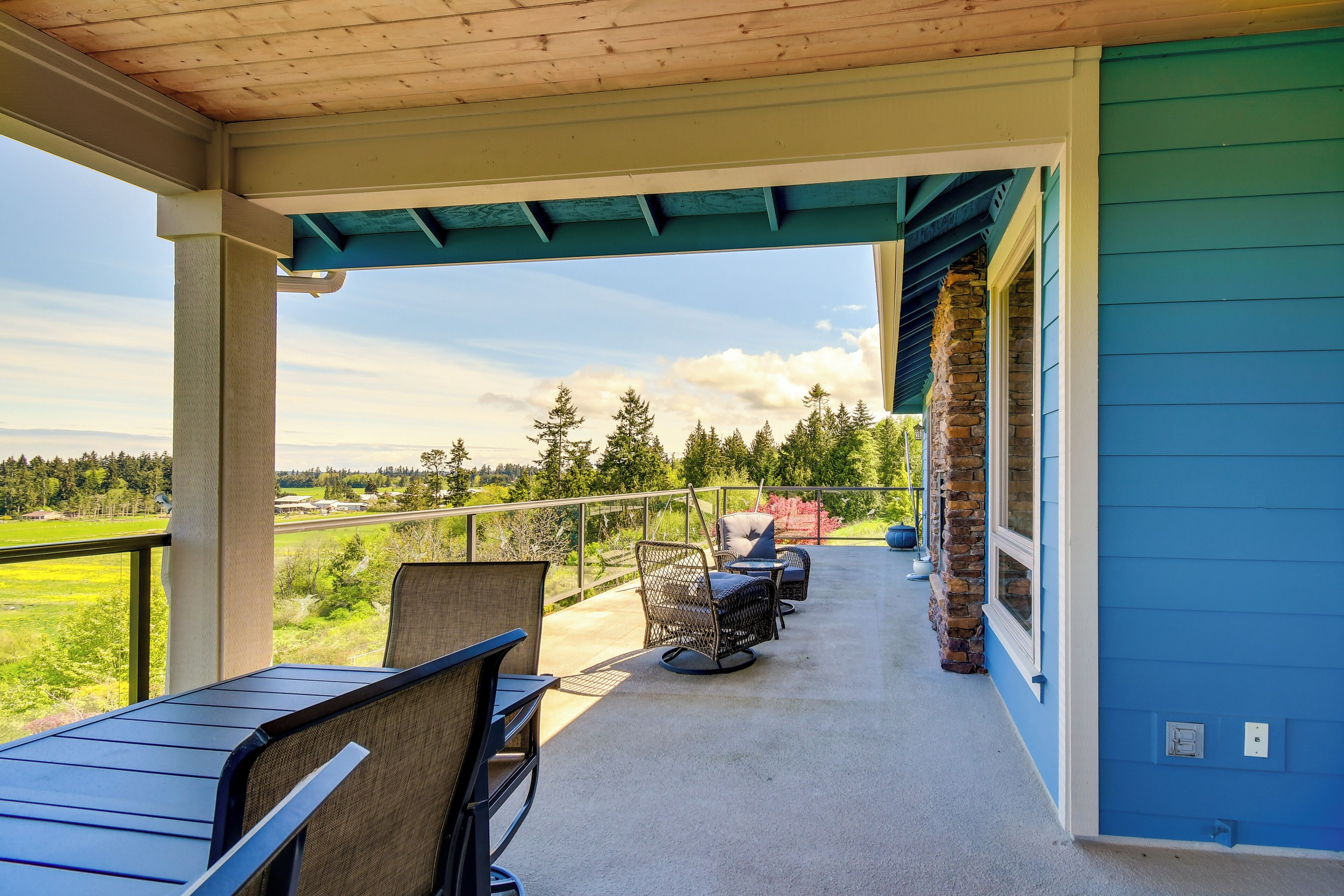 A covered patio with outdoor seating, a stone wall, and a view of the landscape.