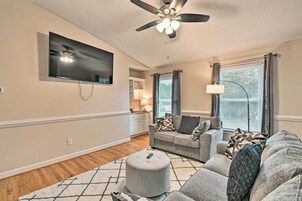A living room with a flat-screen TV, a ceiling fan, a sofa, a coffee table, and a window with curtains.