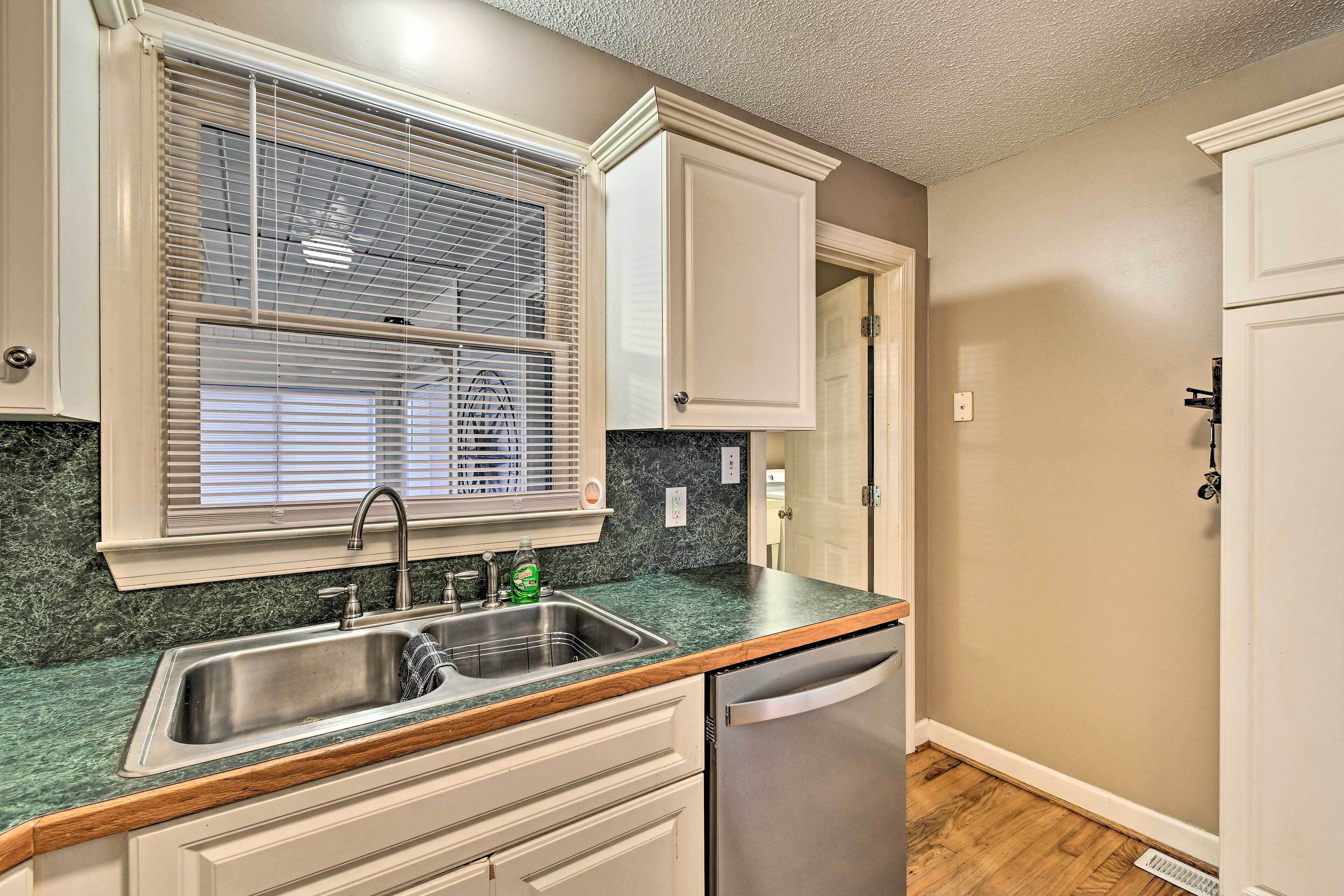 A kitchen with a stainless steel sink, a dishwasher, and a window with blinds.