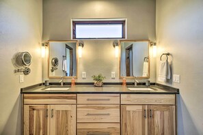 A bathroom with two sinks, wooden cabinets, a small plant, and a window above the mirror. - Pastoral Elgin Escape w/ Covered Patio & Grill! (Elgin)