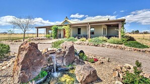 A house with a stone patio, a small waterfall feature, and a clear blue sky. - Pastoral Elgin Escape w/ Covered Patio & Grill! (Elgin)