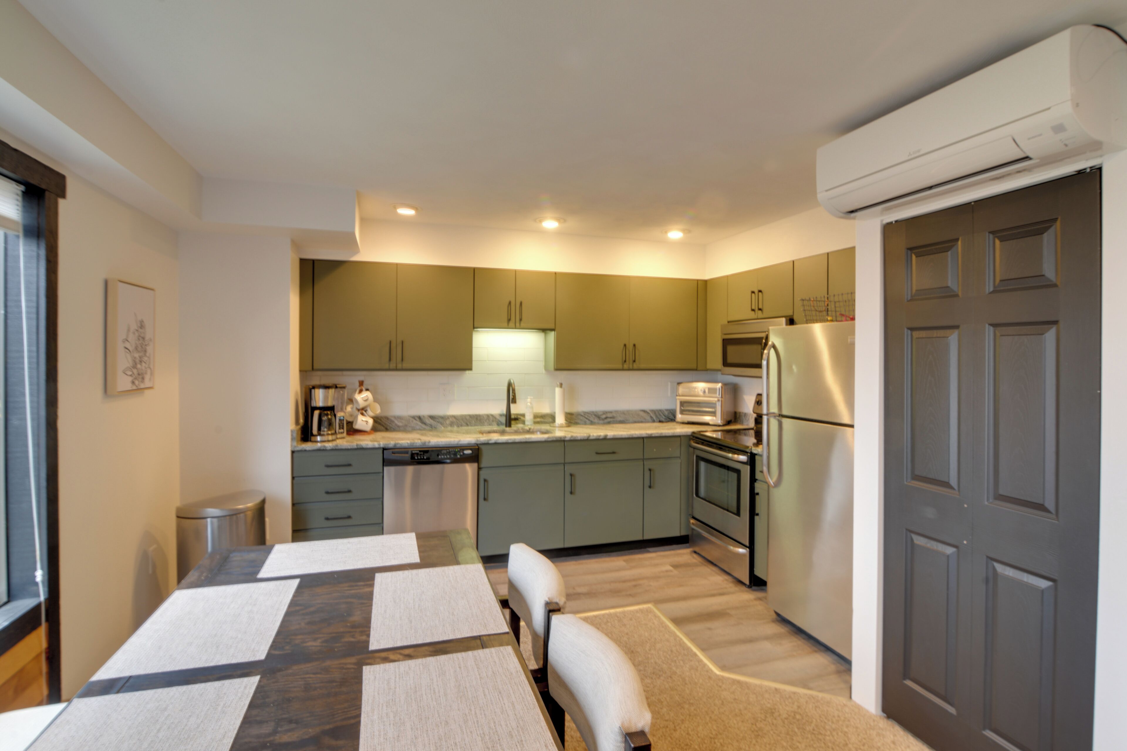 A modern kitchen with green cabinets, a built-in oven, and a refrigerator.
