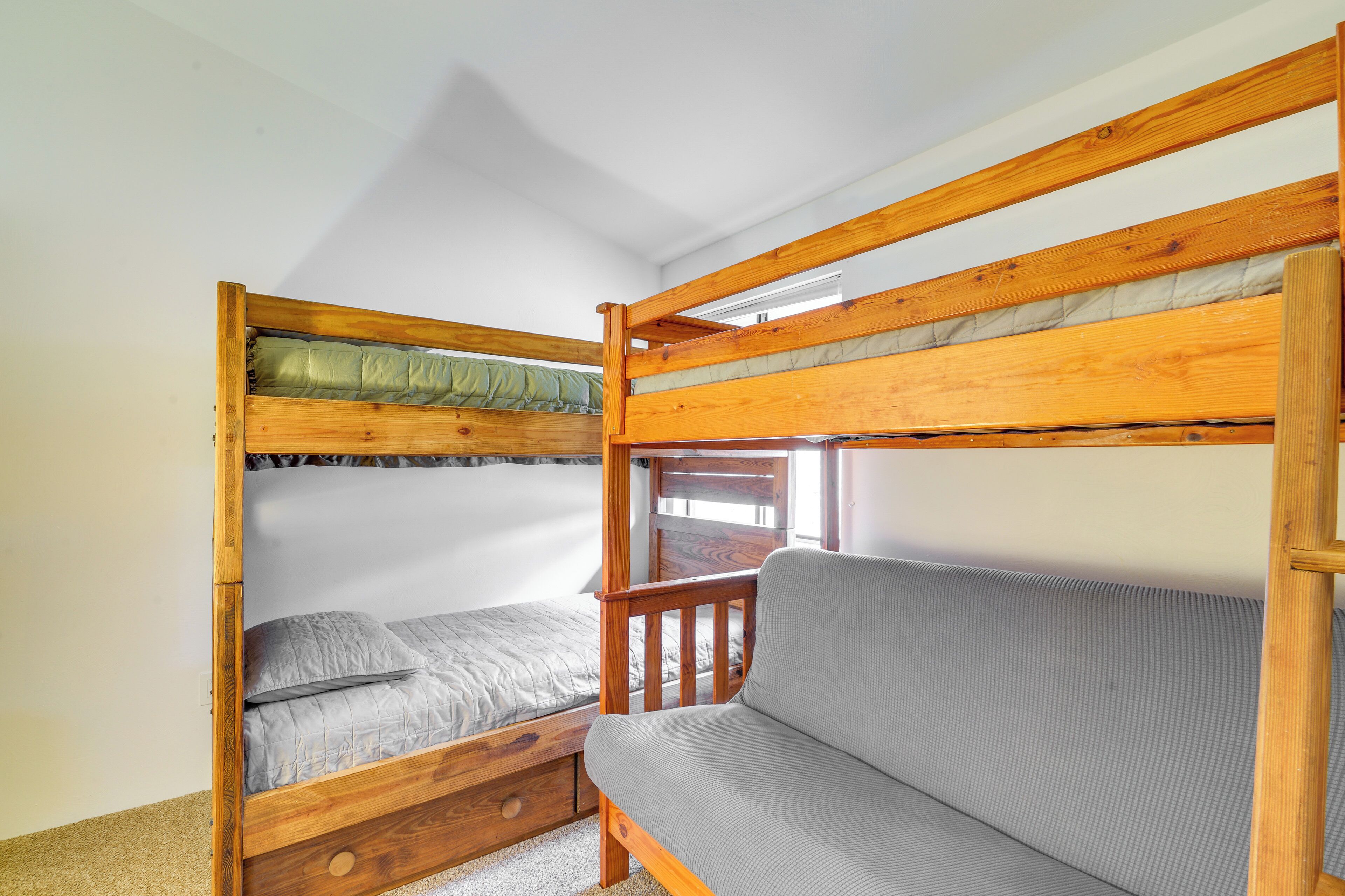 A bunk bed with a wooden frame and a gray mattress, a wooden chair, and a window with natural light.