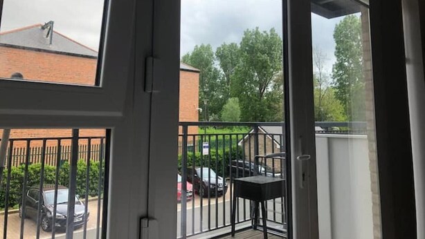 A view from a balcony with a metal railing, a brick building, and parked cars in the background.