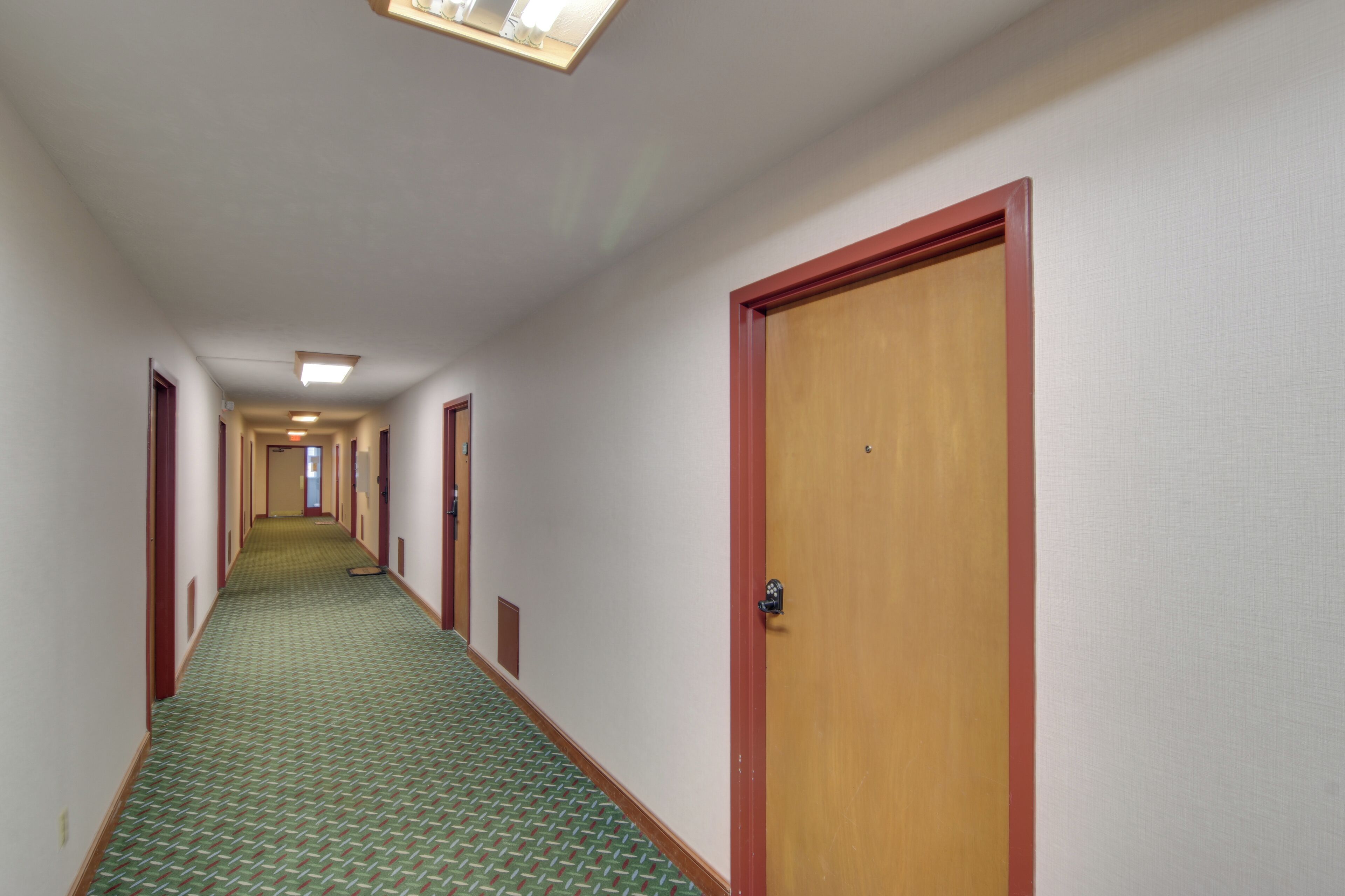 Un couloir d'hôtel avec des revêtements de sol en moquette, des portes en bois et un luminaire au plafond.