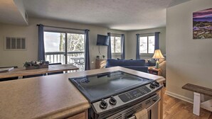 A compact kitchen with a gas stove, a dining table, and a TV mounted on the wall.