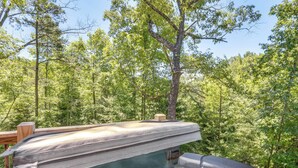 Un jacuzzi en un área boscosa con una terraza de madera y una estructura de piedra.