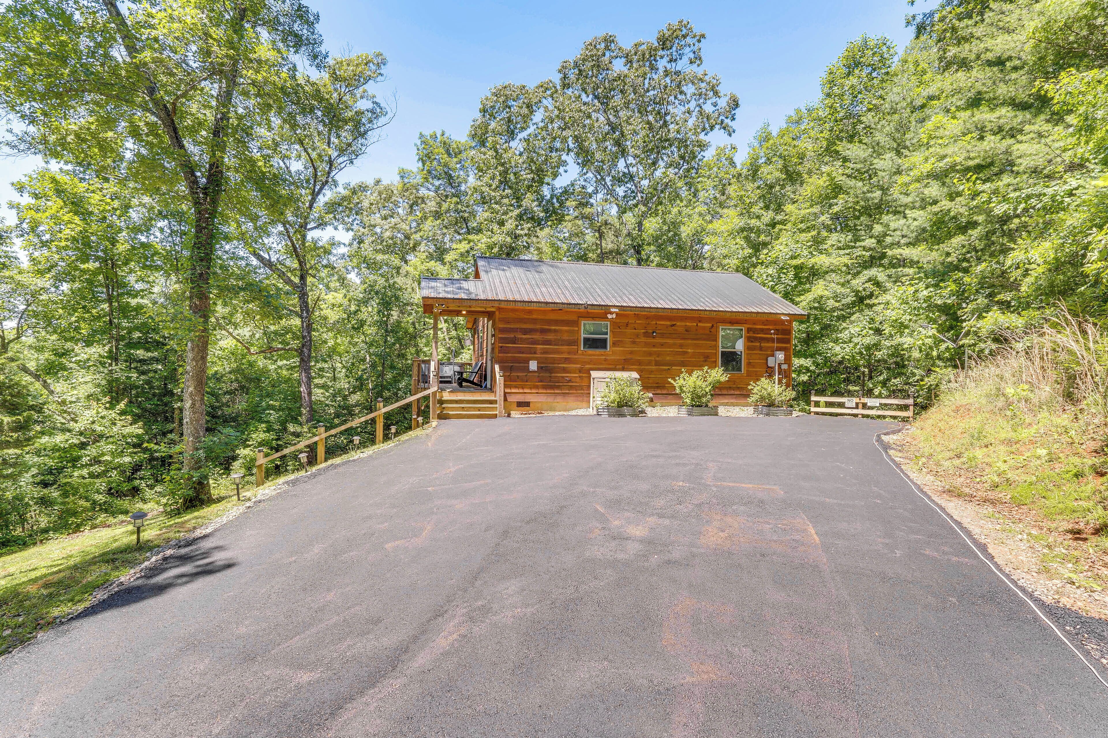 A wooden cabin with a paved driveway, surrounded by trees.