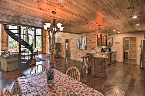 A spacious log cabin interior with a dining area, kitchen, and a spiral staircase leading to a loft bedroom.