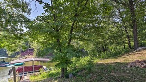 A lakeside cabin with a covered dock, surrounded by dense trees and a clear view of the water. - 'rukarasa Cabin' w/ Yard & Dock at Grand Lake (Eucha)