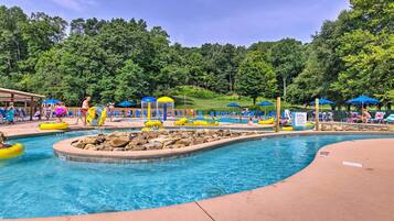 A swimming pool with multiple lanes, surrounded by lounge chairs and umbrellas, set against a backdrop of trees.