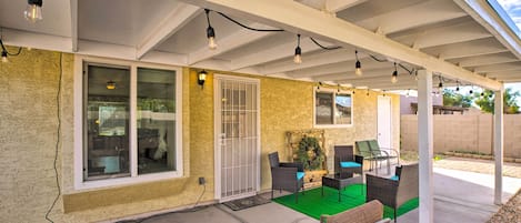 A covered patio with outdoor furniture, a green carpet, and string lights.