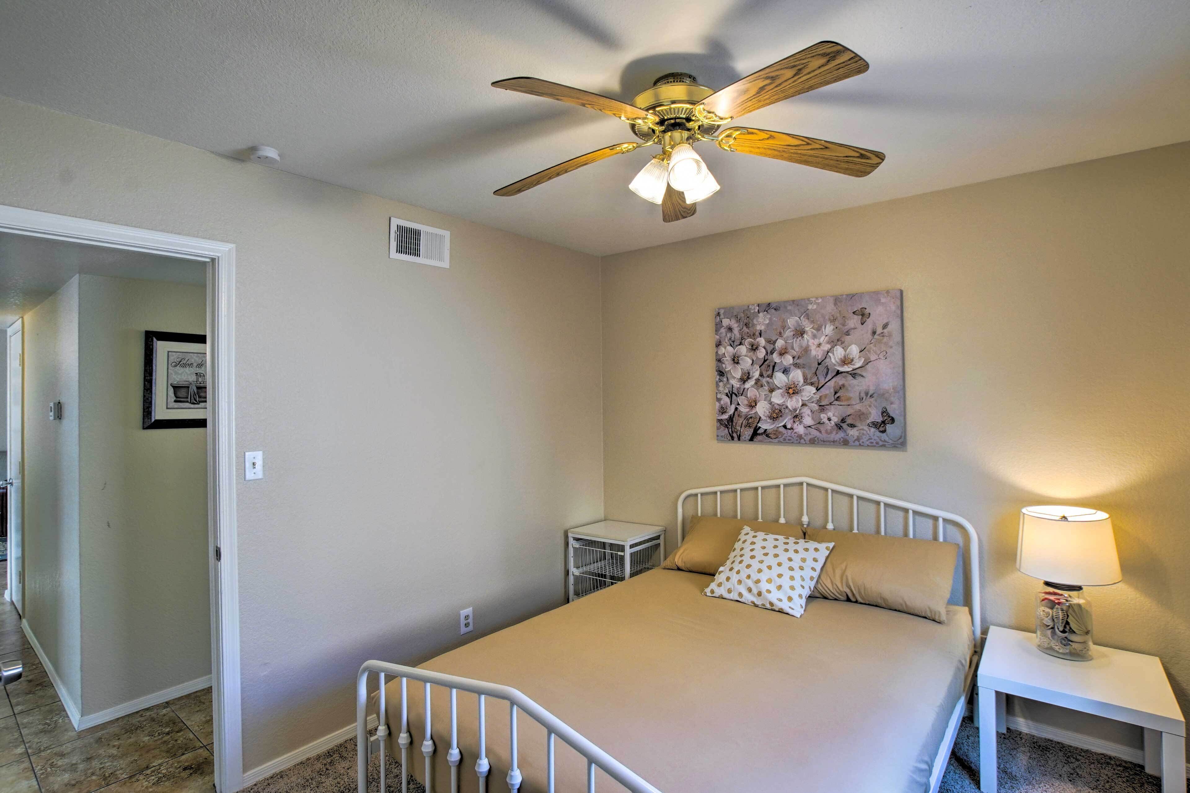 A bedroom with a bed, a ceiling fan, a nightstand with a lamp, and a painting on the wall.
