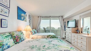 Een slaapkamer met twee bedden, een televisie, een dressoir en een balkon met uitzicht.