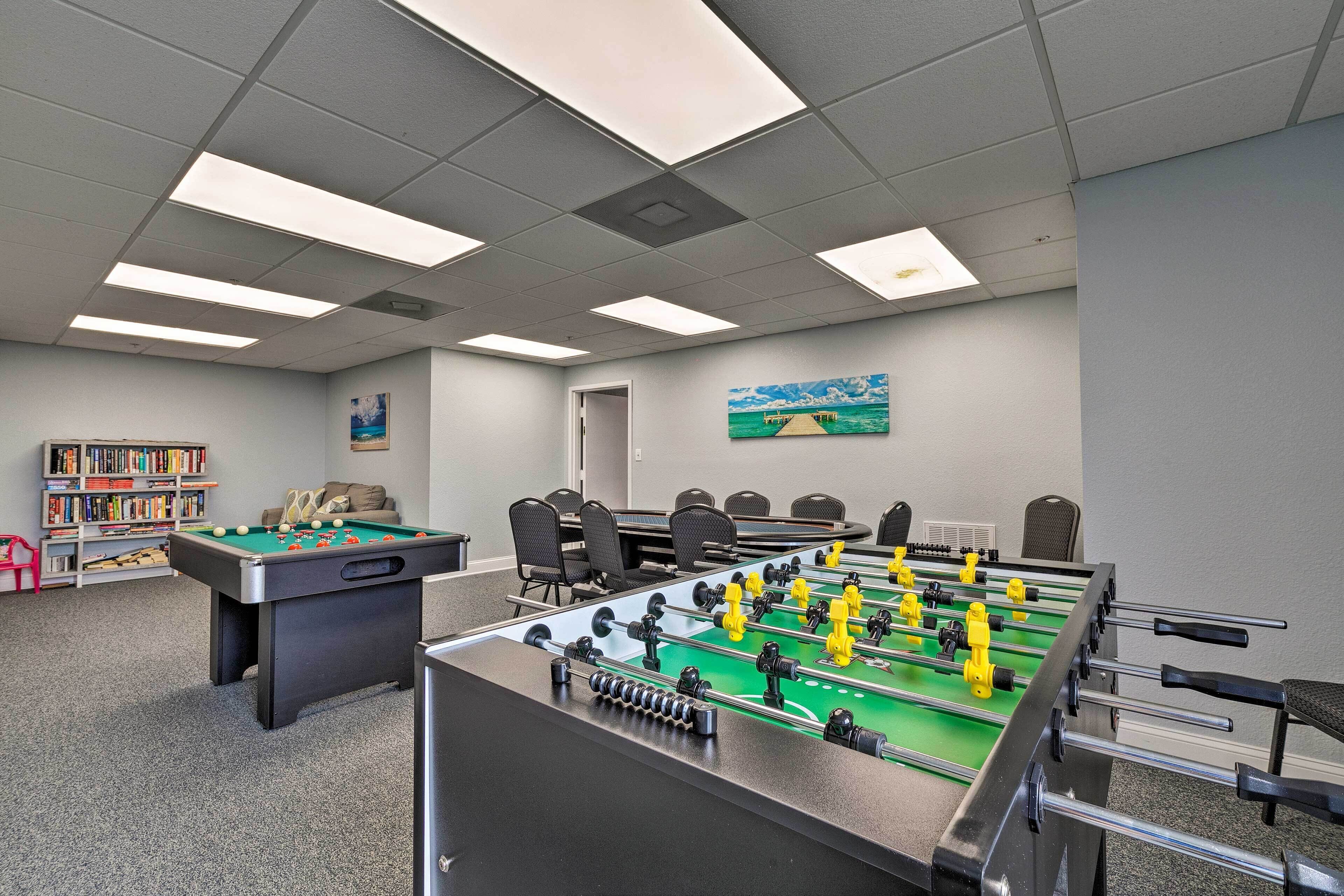 A room with a foosball table, a pool table, and a bookshelf with books.