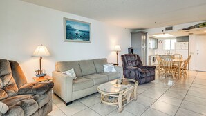 Een woonkamer met een bank, fauteuil en salontafel, een eethoek met een tafel en stoelen, en een keuken op de achtergrond.