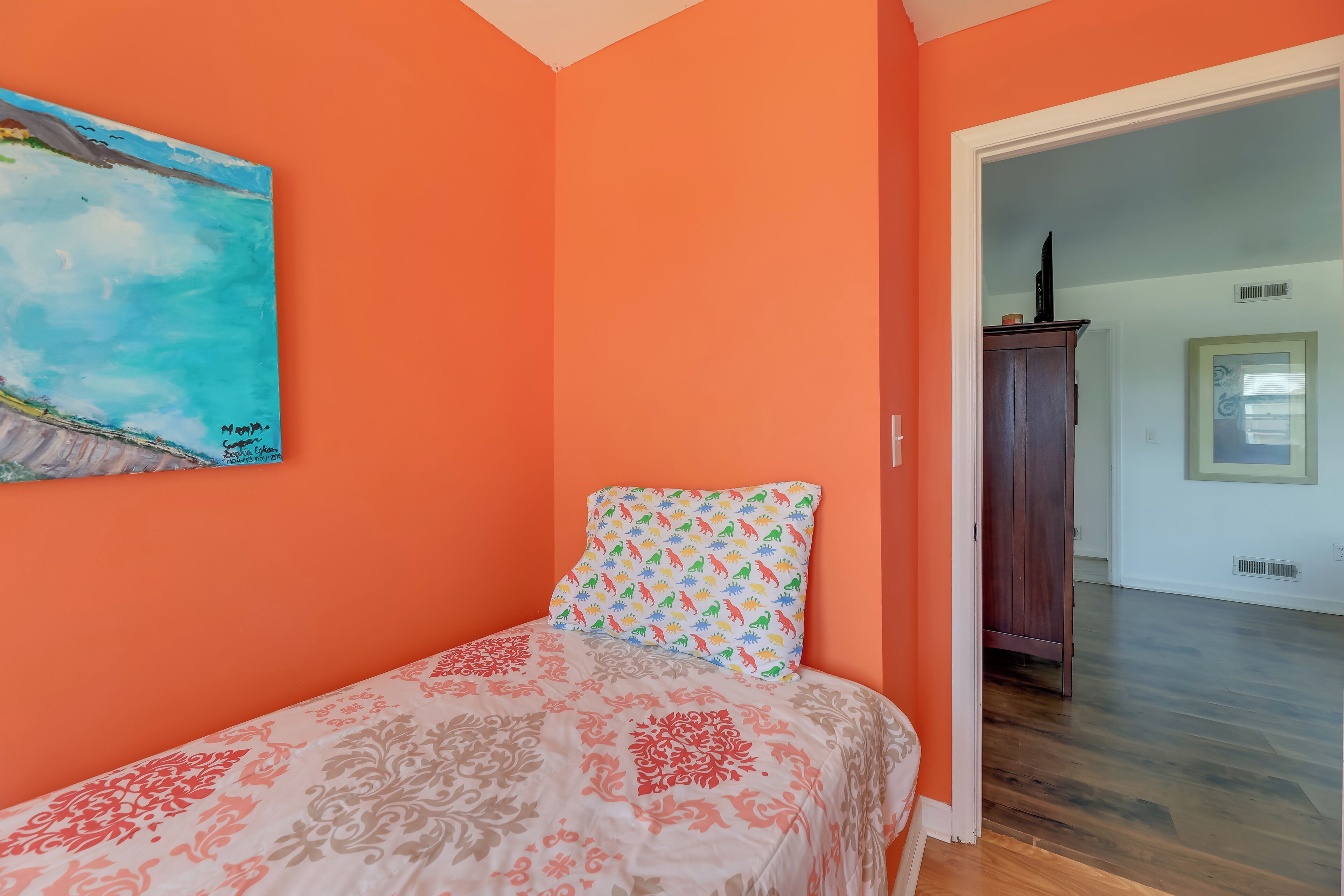 Une chambre à coucher avec un lit, un coussin coloré et un tableau accroché au mur.