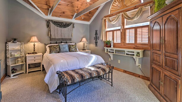 Une chambre à coucher avec un grand lit, deux tables de chevet avec des lampes, un banc, une armoire en bois et une fenêtre avec des volets.