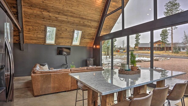 A modern interior with a wooden ceiling, large windows, a glass dining table, and a leather sofa. - Modern Lead A-frame w/ Hot Tub: Hike, Bike & Atv! (Lead)