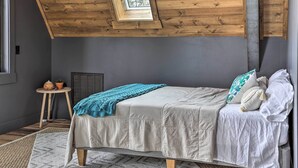 A bedroom with a sloped ceiling, a skylight, a bed with white bedding, a small round table with a plant, and a radiator. - Modern Lead A-frame w/ Hot Tub: Hike, Bike & Atv! (Lead)