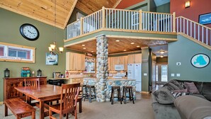 A spacious living area with a wooden dining table, chairs, a stone pillar, and a grey sofa.