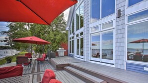 A deck with red chairs and umbrellas, a barbecue, and a view of the water.