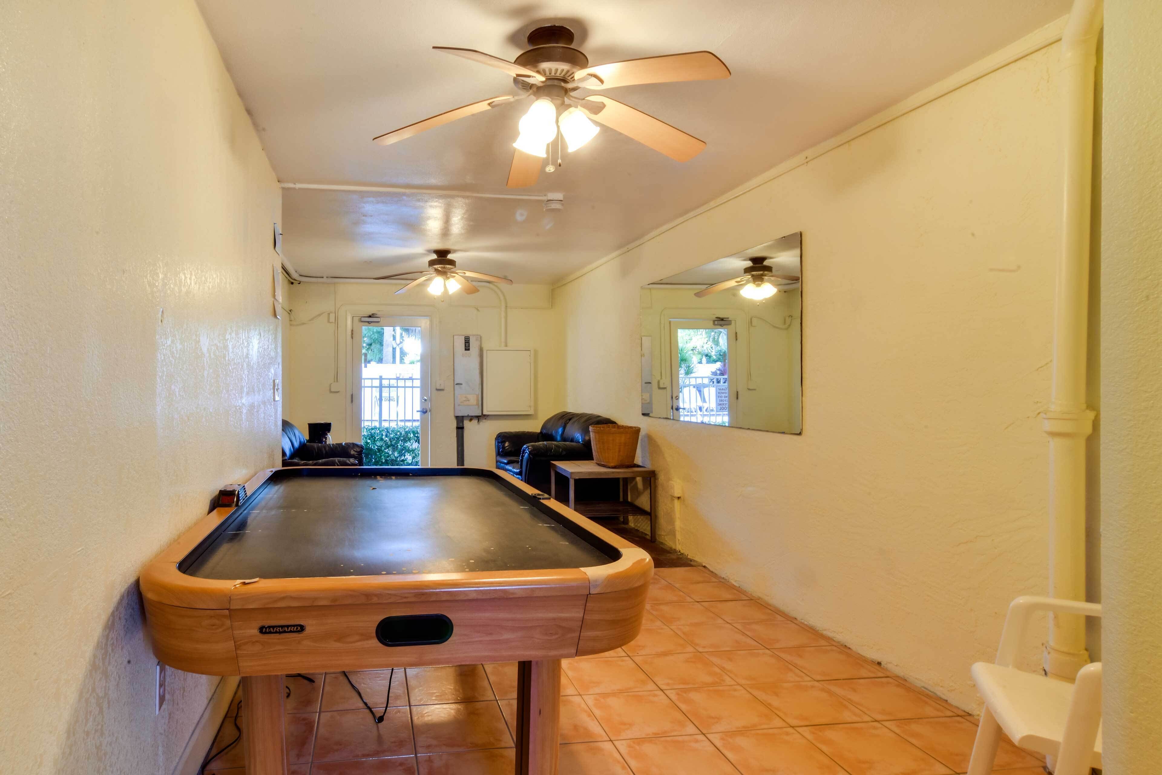 Una mesa de billar en una habitación con ventilador de techo, un espejo en la pared y vistas al exterior.