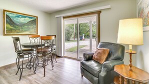 A dining area with a table and chairs, a leather sofa with a lamp, and a painting on the wall.