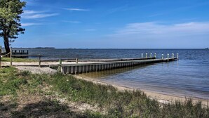 A wooden pier extending into calm water, surrounded by grassy areas and a clear sky. - Charming Painter Home w/ Chesapeake Bay Views (Painter)