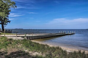 A wooden pier extending into calm water, surrounded by grassy areas and a clear sky.
