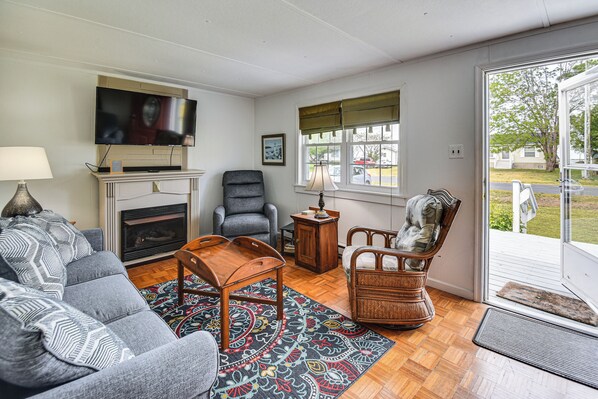 Una sala de estar con sofá, sillón, mesa de centro, chimenea, televisor y vista al exterior.