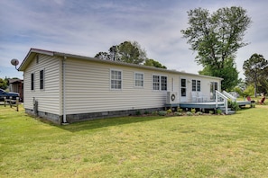 A single-story mobile home with a front porch, a satellite dish, and a small front yard.