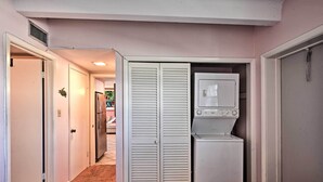 Habitación compacta con lavadora, un refrigerador pequeño y un armario con puertas persianas.