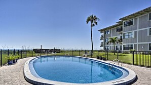 Una piscina con borde de azulejos, rodeada por un patio de ladrillo y una cerca de metal.