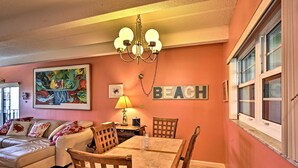 Un área de comedor con una mesa y sillas, una araña, un cuadro y un letrero en la pared que dice "BEACH".