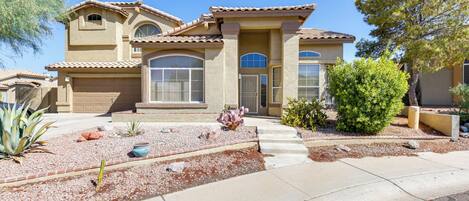 A two-story house with a beige facade, large windows, and a front yard with landscaping.
