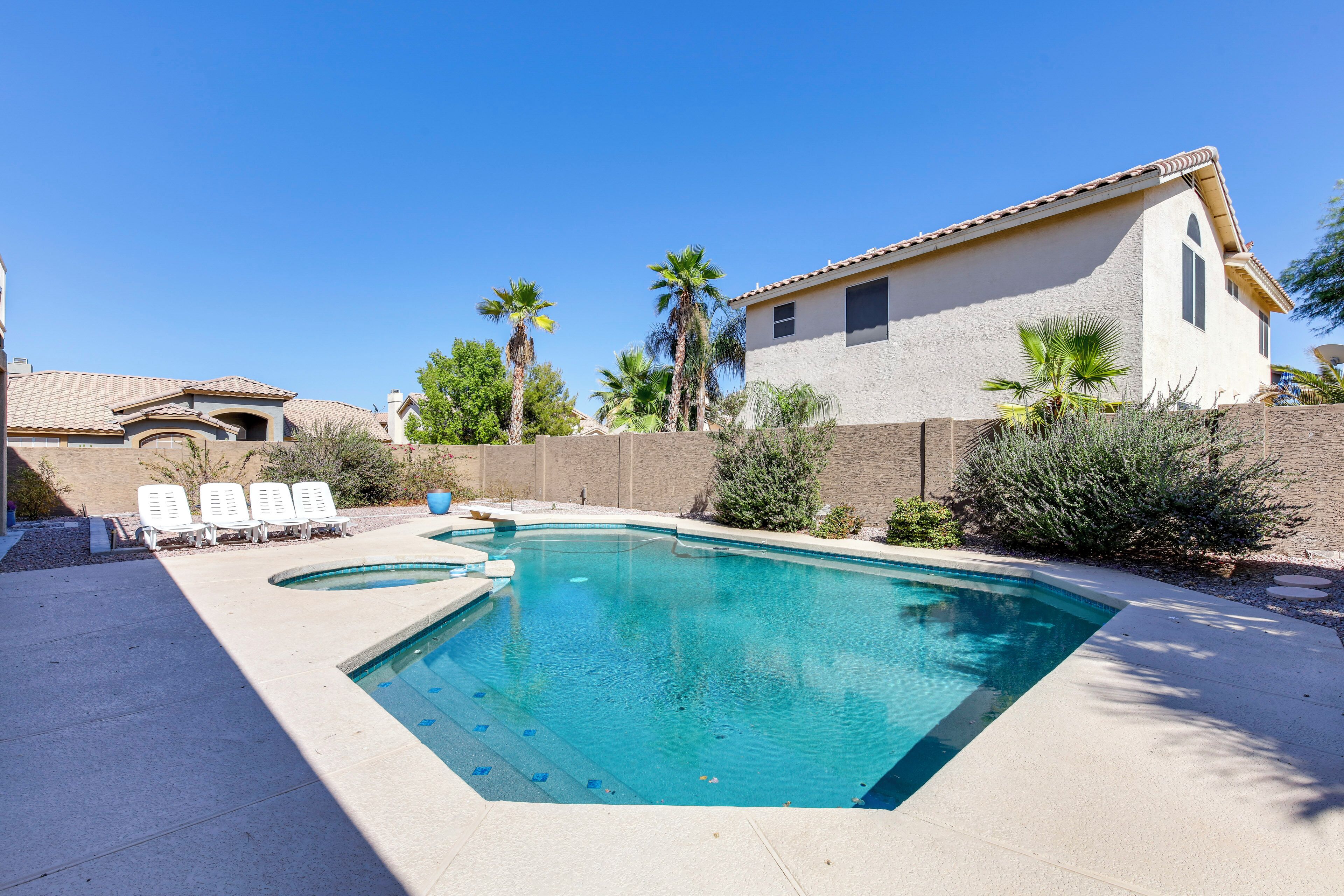 A swimming pool with lounge chairs, surrounded by a house with a tiled roof and palm trees.