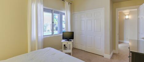A bedroom with a bed, a television on a small table, a white door, and a hallway leading to another room.