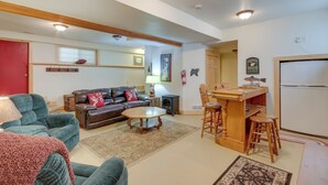 Una sala de estar con sofá, una mesita de centro y una cocina con refrigerador y taburetes de bar.