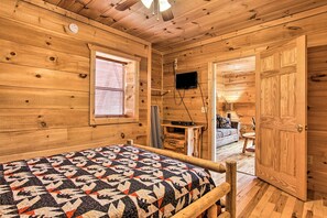 Une pièce de style cabane en bois, avec un lit, un téléviseur fixé au mur et une porte donnant sur une autre pièce.